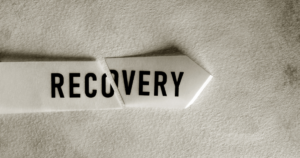 Torn paper strip forming the word RECOVERY on a textured beige surface, symbolizing recovery or renewal.