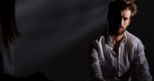 Portrait of a bearded man in a white shirt in moody, low-key lighting with dramatic shadows.