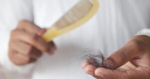 Person brushing hair with a yellow comb, holding a clump of tangled hair in their other hand.